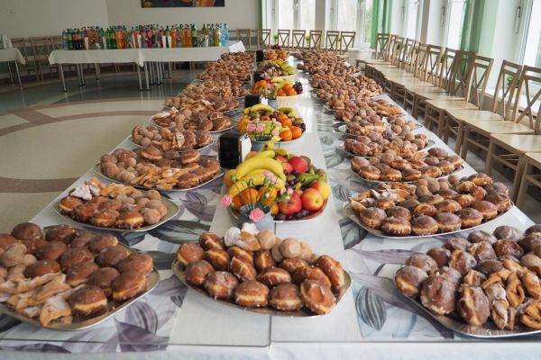 Długi stół z poczęstun kiem dla gości balu zastawiony paterami z pączkami i owocami.