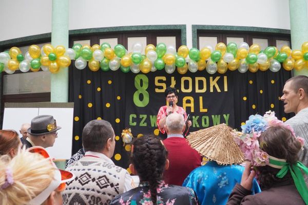 Pani Dyrektor Dps w Lubuczewie wita gości balu stojąc na tle napisu na tle czarnej kotary.