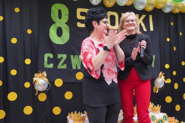 Pani Dyrektor Dps wraz Panią Dyrektor PCPR w Słupsku  w Lubuczewie wita gości balu stojąc na tle napisu, na czarnej kotarze w złote kropki..