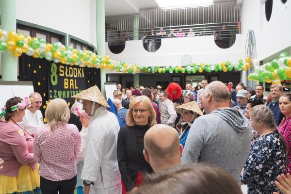 Uczestnicy balu bawiący się na holu domu udekorowanym złotymi, zielonymi i perłowymi balonami.