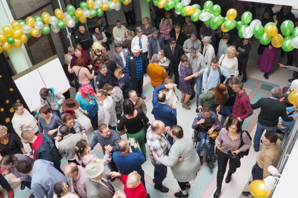 Uczestnicy balu bawiący się na holu domu udekorowanym złotymi, zielonymi i perłowymi balonami.