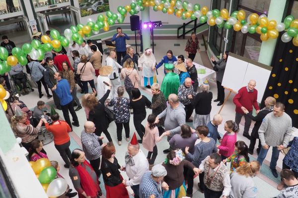 Uczestnicy balu bawiący się na holu domu udekorowanym złotymi, zielonymi i perłowymi balonami.