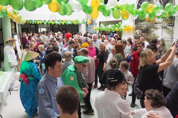Uczestnicy balu bawiący się na holu domu udekorowanym złotymi, zielonymi i perłowymi balonami.