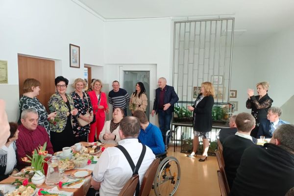 Niektórzy uczestnicy zabawy w Szczypkowicach stoją a niektórzy siedza przy stole.