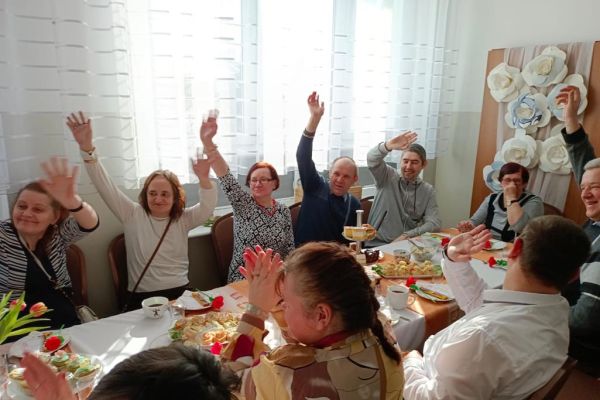 Uczestnicy zabawy w Szczypkowicach przy stole z rękoma machającymi do zdjęcia.
