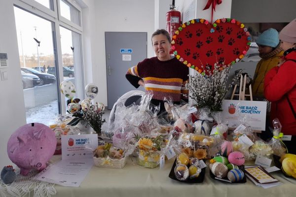 Pani z UTW Rędzikowo oferuje prace na kiermaszu wyłożone na stole w schronisku.