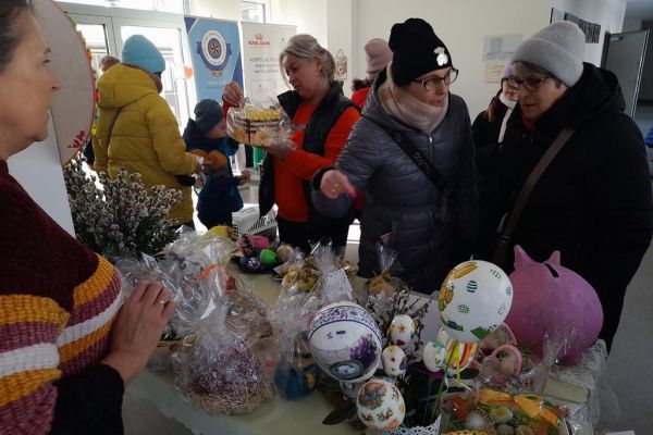 Parę osób przy stoisku kiermaszowym w schronisku stoi i ogląda prace.