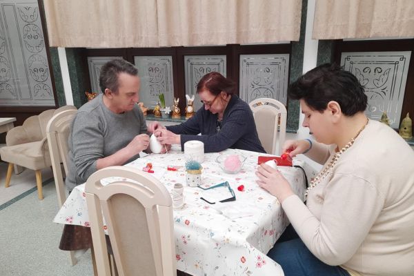 Mieszkańcy siedzą przy stoliku i wyklejają jajka sznyrkiem.