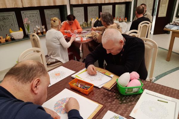 Mieszkańcy wykonują różne czynności siedząc przy stolikach w terapii.