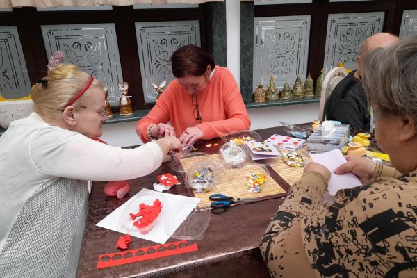 Mieszkańcy wykonują różne czynności siedząc przy stolikach w terapii.