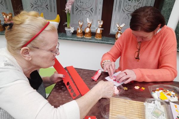 Mieszkańcy wykonują różne czynności siedząc przy stolikach w terapii.