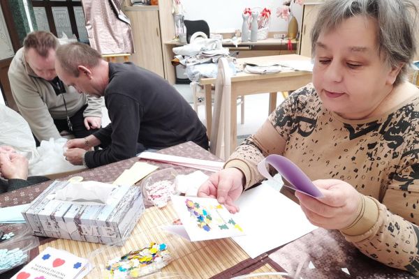 Mieszkańcy wykonują różne czynności siedząc przy stolikach w terapii.