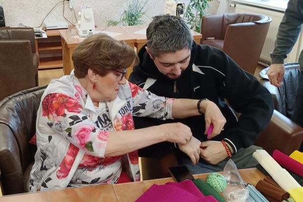 Mieszkańcy wraz z uczestnikami UTW z Redzikowa wykonują ozdoby siedząc przy stolikach w kawiarence na terenie DPS  w Lubuczewie.