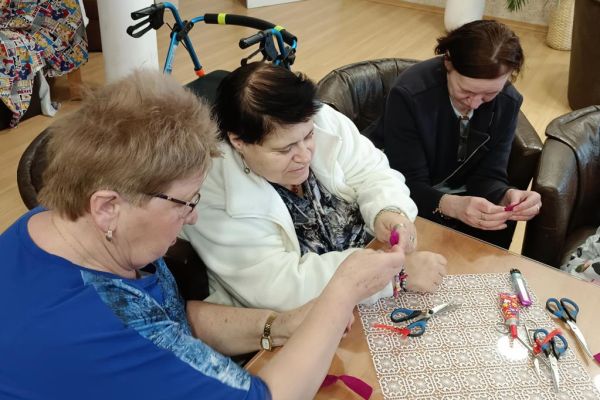 Mieszkańcy wraz z uczestnikami UTW z Redzikowa wykonują ozdoby siedząc przy stolikach w kawiarence na terenie DPS  w Lubuczewie.