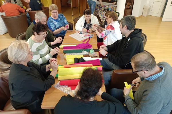 Mieszkańcy wraz z uczestnikami UTW z Redzikowa wykonują ozdoby siedząc przy stolikach w kawiarence na terenie DPS  w Lubuczewie.