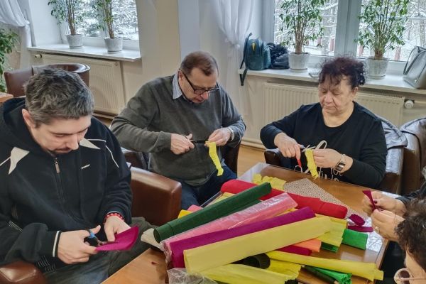 Mieszkańcy wraz z uczestnikami UTW z Redzikowa wykonują ozdoby siedząc przy stolikach w kawiarence na terenie DPS  w Lubuczewie.