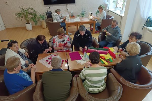Mieszkańcy wraz z uczestnikami UTW z Redzikowa wykonują ozdoby siedząc przy stolikach w kawiarence na terenie DPS  w Lubuczewie.