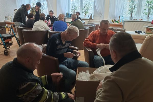 Mieszkańcy wraz z uczestnikami UTW z Redzikowa wykonują ozdoby siedząc przy stolikach w kawiarence na terenie DPS  w Lubuczewie.