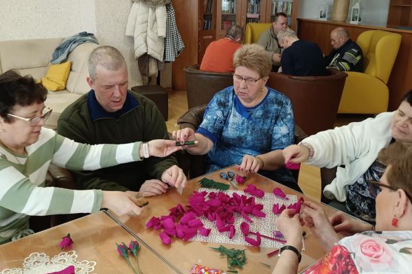 Mieszkańcy wraz z uczestnikami UTW z Redzikowa wykonują ozdoby siedząc przy stolikach w kawiarence na terenie DPS  w Lubuczewie.