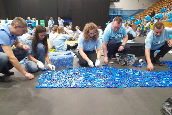 Mieszkańcy wraz z wolontariuszami układają serce dla z nakrętek.