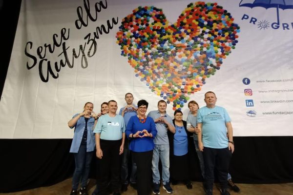 Mieszkańcy wraz z dwona pracownicami domu i Panią Dyrektor pod banerem promującym akcje serce dla autyzmu.