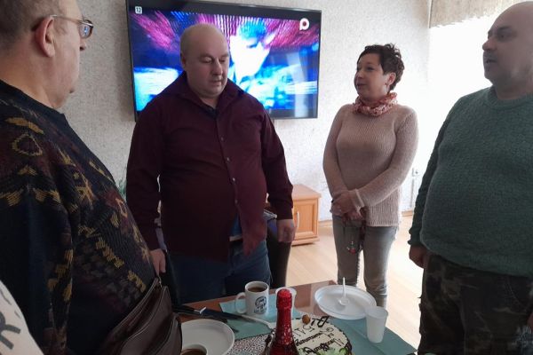 Kilku mieszkańców wraz z solenizantem świętują jego urodziny i imieniny przy stolikach w kawiarence i przy słodkościach i napojach oraz torcie.