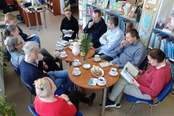 Mieszkańcy w bibliotece przy stolikach omawiają książki.