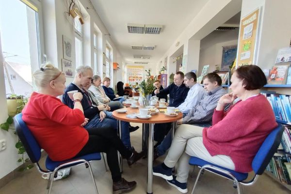 Mieszkańcy w bibliotece przy stolikach omawiają książki.