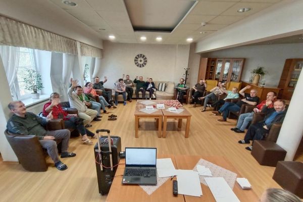 mieszkańcy siedza w fotelach na około sali i uczestniczą w quizie.