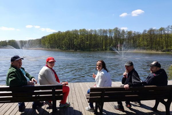 Mieszkańcy zwiedzają Złotów. Siedzą na ławkach przy jeziorze.
