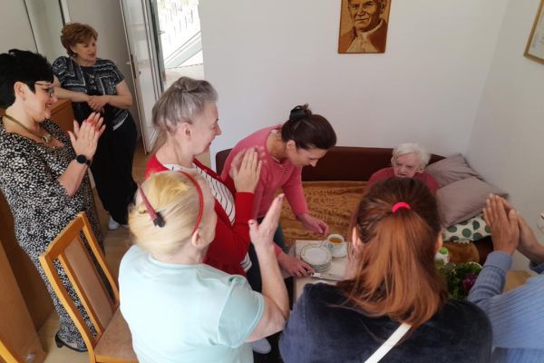 Mieszkanki klaszczą a pracownica kroi tort.