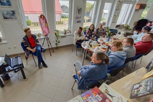 Mieszkańcy siedzą przy stolikach w bibliotece i uczestniczą w spotkaniu DKK.