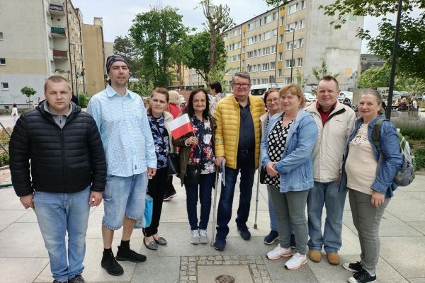 Mieszkańcy w parku w Słupsku podczas Dnia Godności Osób z Niepełnosprawnością Intelektualną stoją w grupowym zdjęciu z panem sędzią sportowym Romualdem Rasiakiem.