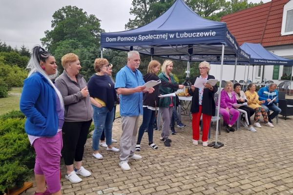 Uczestnicy pikniku śpiewają na stojąco na tarasie.