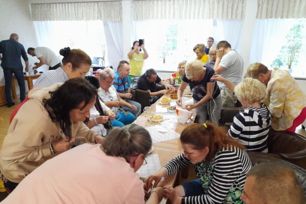 Mieszkańcy wraz z uczestnikami UTW z Redzikowa przywiązują sznurki do poidełek dla ptaków siedząc przy stolikach w kawiarence domu.