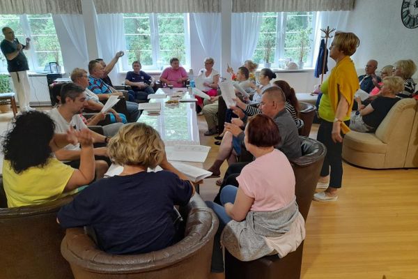 Mieszkańcy wraz z uczestnikami UTW z Redzikowa wspólnie śpiewają piosenki siedząc przy stolikach w kawiarence domu.