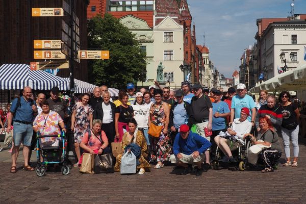 Mieszkańcy wraz z pracownikami domu w Toruniu pod pomnikiem - zdjęcie grupowe.