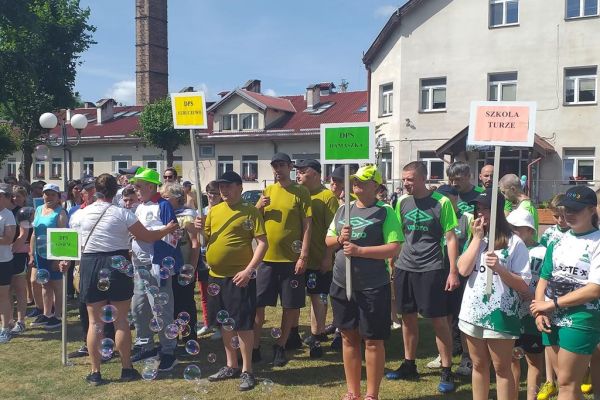 Mieszkańcy stoją podczas defilady na olimpiadzie sportowej w DPS w Damaszce wśród innych uczestników zawodów sportowych.