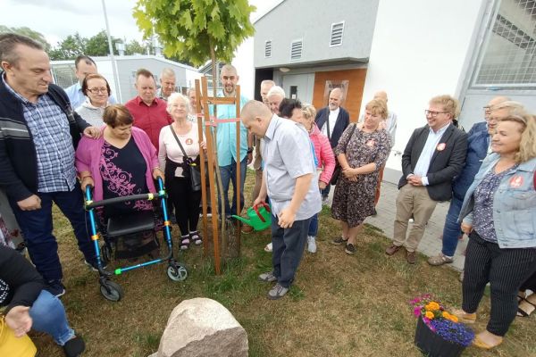 Mieszkaniec podlewa drzewko obok stoją uczestnicy UTW i inni uczestnicy projektu.