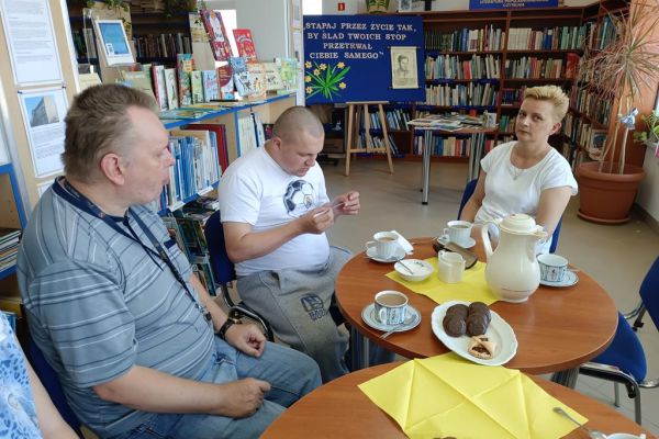 Mieszkańcy na spotkaniu DKK w Objeździeb czytają poezję Szymborskiej siedząc przy stolikach.