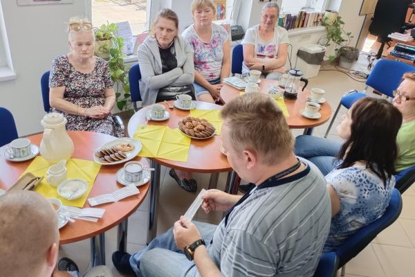 Mieszkańcy na spotkaniu DKK w Objeździeb czytają poezję Szymborskiej siedząc przy stolikach.