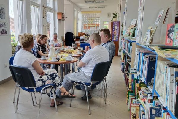 Mieszkańcy na spotkaniu DKK w Objeździeb czytają poezję Szymborskiej siedząc przy stolikach.