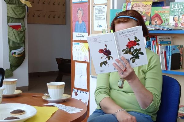 Mieszkanka na spotkaniu DKK w Objeździeb czytają poezję Szymborskiej siedząc przy stoliku.