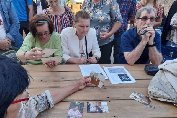 Mieszkanki i inni uczestnicy spaceru oglądaja pamiatkowe zdjęcia.