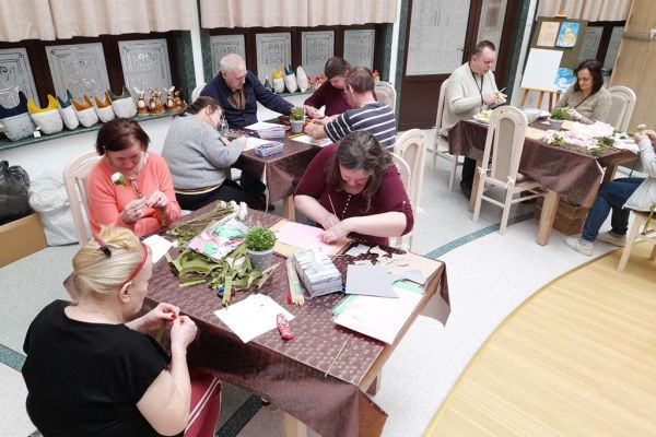 Mieszkańcy na pierwszym planie wycinaja w bibule listki a na dalszym ubijaja ciasto.