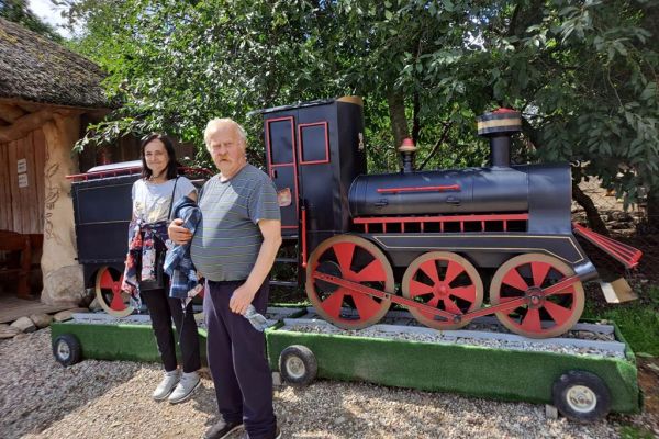 Dwoje mieszkańców na tle lokomotywy w parku miniatur.