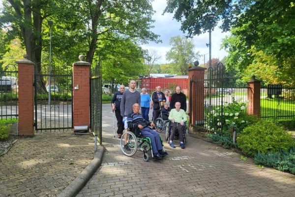 Mieszkańcy wychodza przez bramę DPS na spacer grupowy.