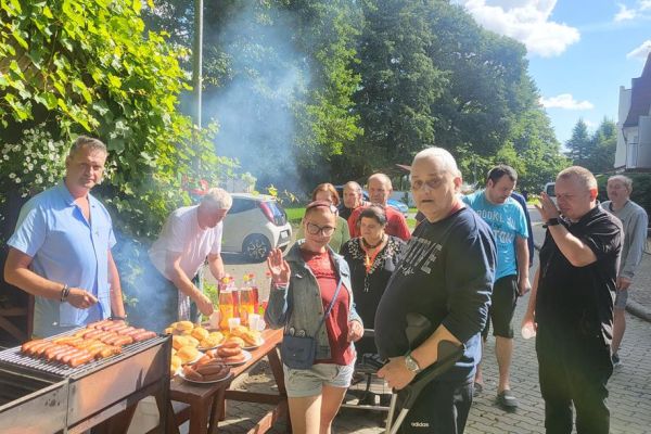 Mieszkańcy stoją przy rozpalonym grillu.