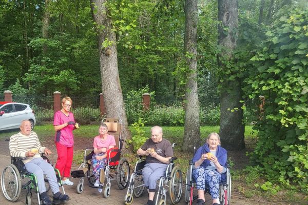 Mieszkańcy poruszający się na wózkach inwalidzkich siedzą i konsumują kiełbaski z grilla.