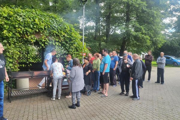 Mieszkańcy stoją przy rozpalonym grillu.